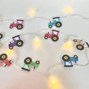 May include: A string of fairy lights with colorful tractor-shaped ornaments. The lights are white and the tractors are red, blue, green, yellow, purple, and orange.