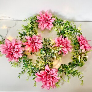 Può includere: Una ghirlanda di fiori di seta rosa con foglie verdi. I fiori sono disposti in cerchio e sono circondati da foglie verdi. La ghirlanda è perfetta per un matrimonio primaverile o estivo.
