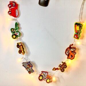 May include: A string of construction vehicle-themed fairy lights with yellow bulbs. The vehicles are red, green, yellow, and orange.