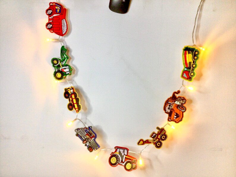 May include: A string of construction vehicle-themed fairy lights with yellow bulbs. The vehicles are red, green, yellow, and orange.