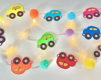May include: A colorful car-themed garland with felt car cutouts in various colors, including yellow, blue, and pink. The garland also features pom-poms and small, warm white LED lights, creating a festive and playful decoration.