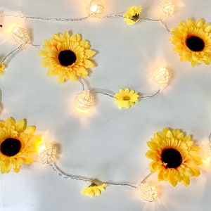 Puede incluir: Una cadena de luces blancas con decoraciones en forma de girasol amarillo y bombillas de jaula de alambre blanco.