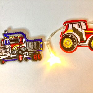 May include: A string of fairy lights with a red and yellow tractor and a blue and red dumper truck attached. The lights are white and the truck and tractor are embroidered.