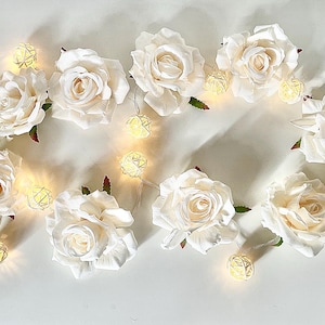 Peut inclure: Des roses artificielles blanches avec de petites lumières rondes blanches enfilées entre elles. Les lumières sont sur une chaîne de fil et ont une lueur blanc chaud.