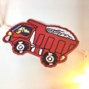 May include: Red toy truck with a white driver and a white load of gravel in the back. The truck has black wheels and a yellow light on the front.