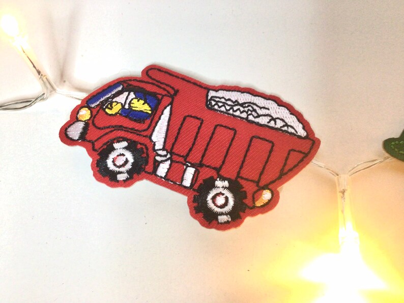 May include: Red toy truck with a white driver and a white load of gravel in the back. The truck has black wheels and a yellow light on the front.