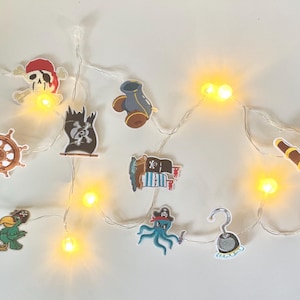 Peut inclure: Une guirlande lumineuse avec des découpes en papier sur le thème des pirates, dont un perroquet, un coffre au trésor, un gouvernail, un chapeau de pirate, une longue-vue et une botte de pirate. Les lumières sont alimentées par piles et ont une lueur blanc chaud.