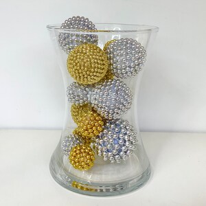 K&ouml;nnte beinhalten: Eine klare Glasvase gef&uuml;llt mit silbernen und goldenen Dekorationskugeln. Die Kugeln bestehen aus kleinen Perlen und haben eine strukturierte Oberfl&auml;che.