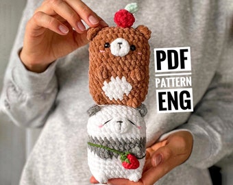 May include: Two crocheted stuffed animals stacked on top of each other. The top animal is a brown bear with a red berry on its head. The bottom animal is a white panda with a gray and white striped body. The animals are holding red berries in their paws. The text "PDF PATTERN ENG" is visible in the image.