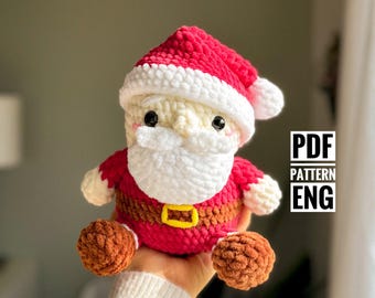 May include: A handmade crochet Santa Claus doll. The doll has a red hat with white trim, a white beard, and a red suit with a yellow belt. The doll's feet are brown. The text "PDF PATTERN ENG" is visible.
