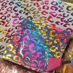 May include: A close-up of a black and iridescent resin casting with a leopard print design. The resin is being smoothed with a pink tool.