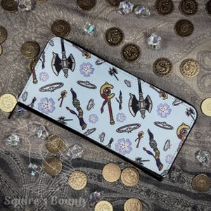 May include: A light blue wallet with a black zipper, featuring a repeating pattern of axes, staves, flowers, and jewelry. The wallet is surrounded by gold coins and clear crystals.