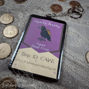 May include: A black and purple Squire's Bounty employee ID badge with a crow illustration and the text "Squire Head Crow." The badge is attached to a silver keychain. Gold coins are scattered around the badge.