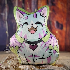 May include: A plush toy shaped like a cat with purple wings and a heart on its chest. The cat is smiling and has a light blue and green color scheme.