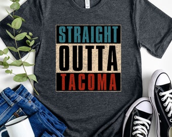 May include: Heather dark grey t-shirt featuring the text "STRAIGHT OUTTA TACOMA" in a vintage style graphic. The shirt is shown against a white background with jeans, a mug, and black trainers.