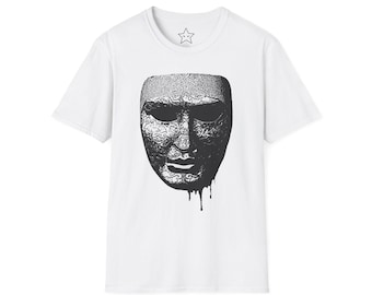 May include: White t-shirt featuring a detailed black and white mask design. The mask has intricate patterns and a dripping effect at the bottom. The shirt has a crew neck and a small star logo near the collar.