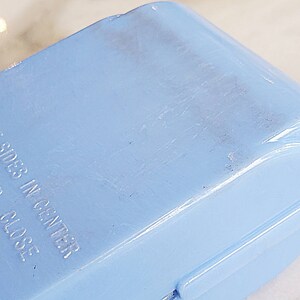 May include: A light blue plastic container with the text "Sides In Center To Close" embossed on the side.