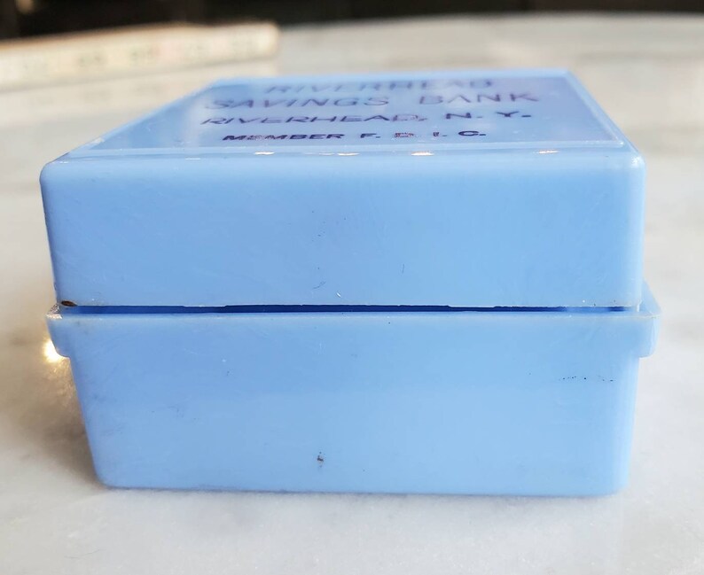 May include: A light blue plastic box with the text "Riverhead Savings Bank Riverhead, N.Y. Member F.D.I.C." printed on the top.