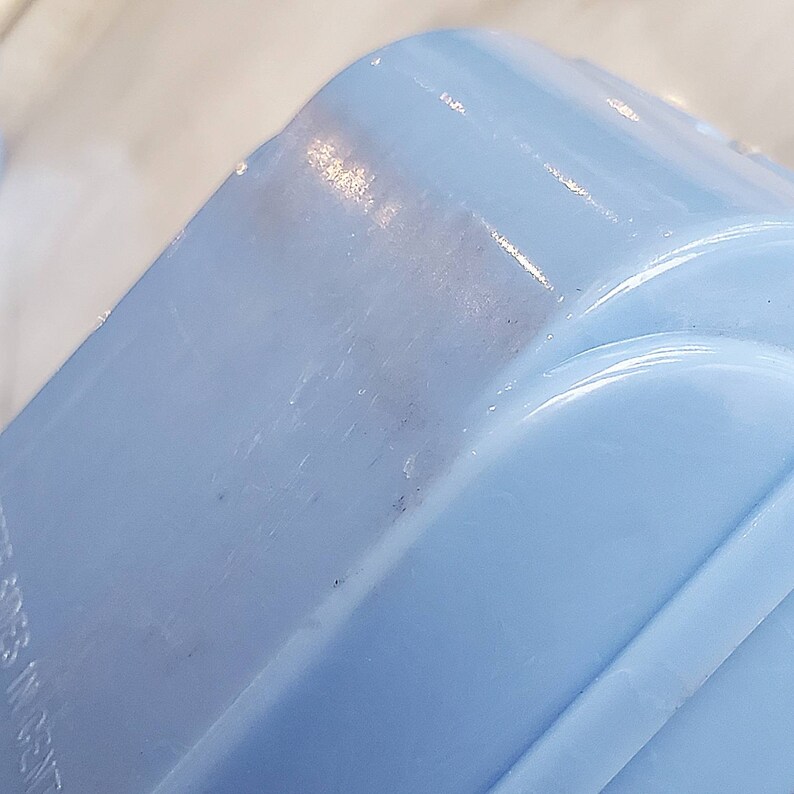 May include: A close-up of a light blue plastic container with a smooth, shiny surface. The container has a rounded shape and a slight curve on the top.