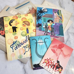 May include: A collection of vintage cards with colorful illustrations. One card features a couple with a farewell message, another shows a donkey pulling a carriage, and a third card has a harp design. The cards are on a marble surface.