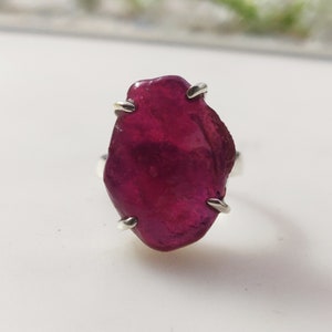 May include: A ring featuring a large, irregularly shaped, deep red ruby gemstone set in a silver band.