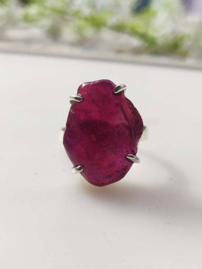 May include: A ring featuring a large, irregularly shaped, deep red ruby gemstone set in a silver band.