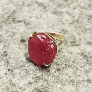 Pode incluir: Um anel de prata com uma grande gema de rubi vermelho facetado.