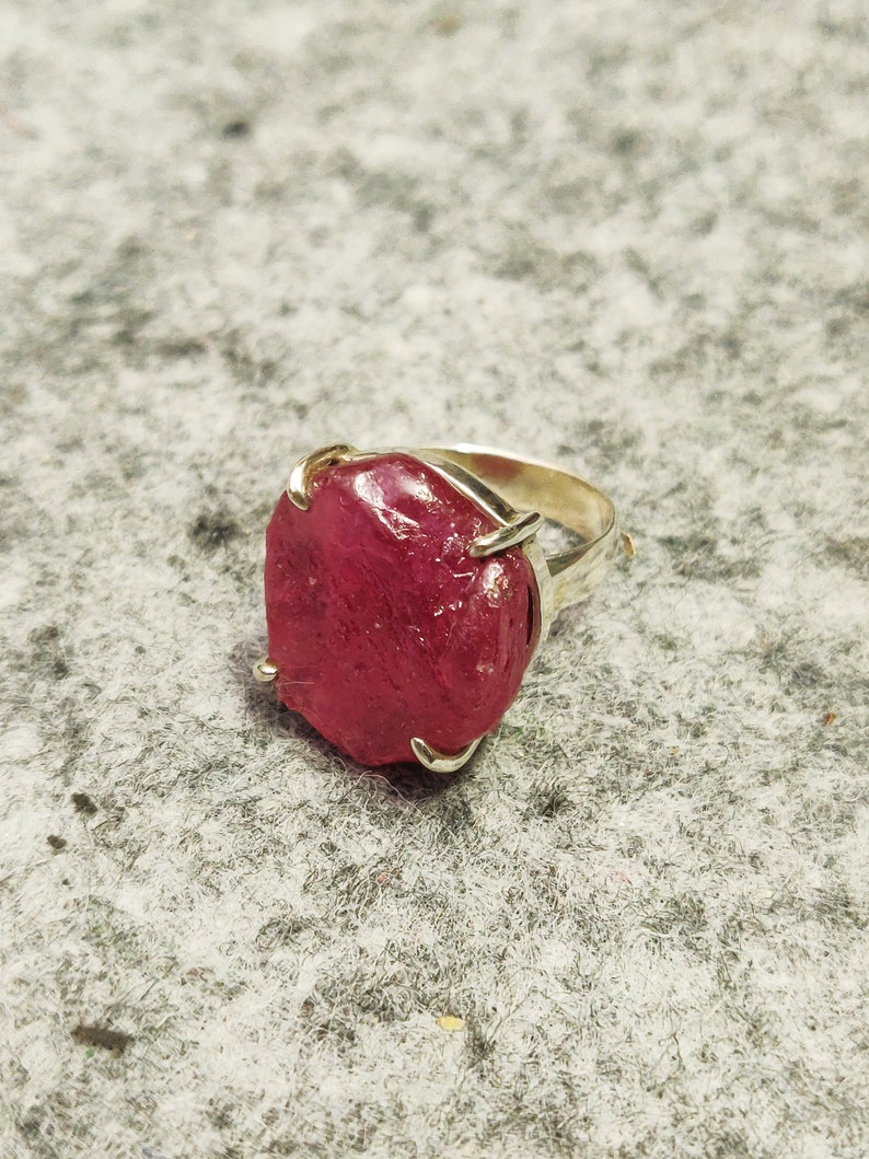 Pode incluir: Um anel de prata com uma grande gema de rubi vermelho facetado.