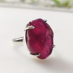 May include: A silver ring featuring a large, deep red, faceted gemstone set in a claw setting.