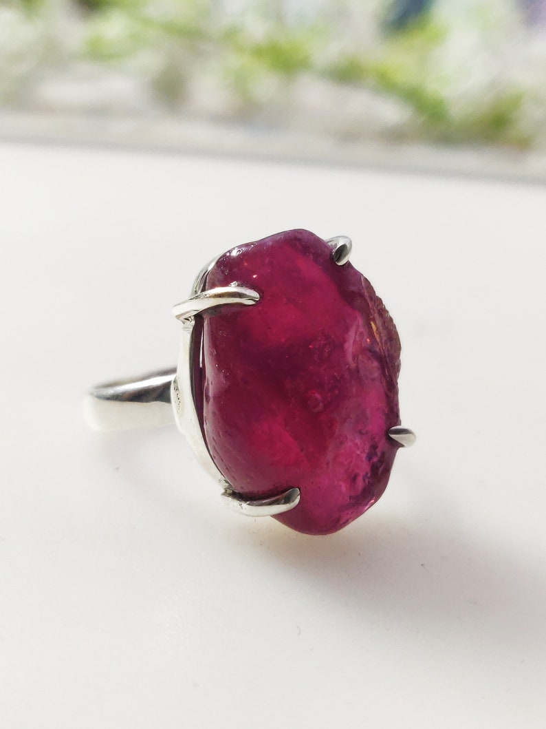 May include: A silver ring featuring a large, deep red, faceted gemstone set in a claw setting.