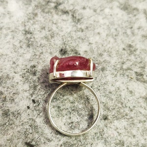 Pode incluir: Um anel de prata com uma grande gema rosa facetada engastada em uma moldura de bezel.