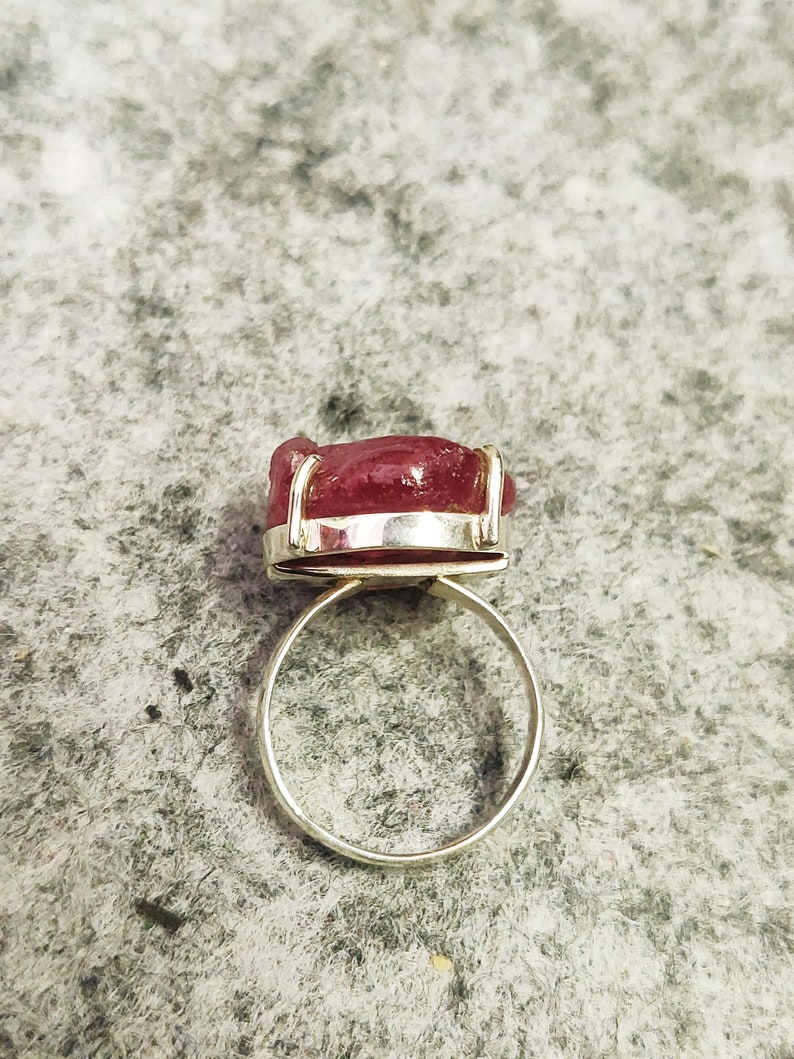 Pode incluir: Um anel de prata com uma grande gema rosa facetada engastada em uma moldura de bezel.