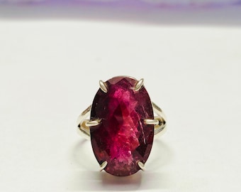 May include: A silver ring with a large, oval-shaped, deep pink gemstone.