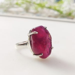 May include: A silver ring featuring a large, irregularly shaped, deep pink gemstone.
