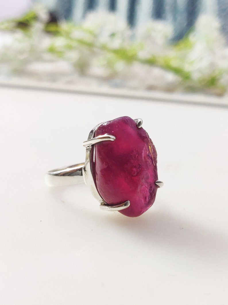 May include: A silver ring featuring a large, irregularly shaped, deep pink gemstone.