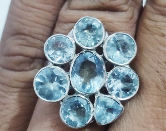 May include: A silver ring with a cluster of eight light blue gemstones set in a flower shape.