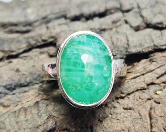 May include: A silver ring with a large, oval-shaped green gemstone. The ring is set on a wooden surface.
