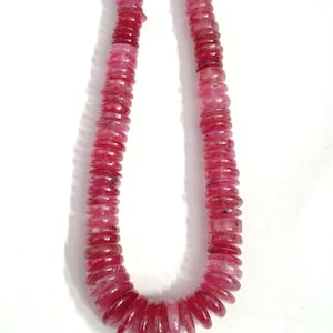 May include: A strand of circular, disc-shaped beads in varying shades of deep pink and magenta. The beads are translucent with natural inclusions and are strung together in a U-shape, creating a continuous line of polished, flat-edged gemstone pieces.