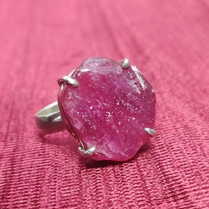 Pode incluir: Um anel de prata com uma grande gema de rubi bruto. O rubi &eacute; de cor rosa intenso e tem uma textura &aacute;spera e natural.