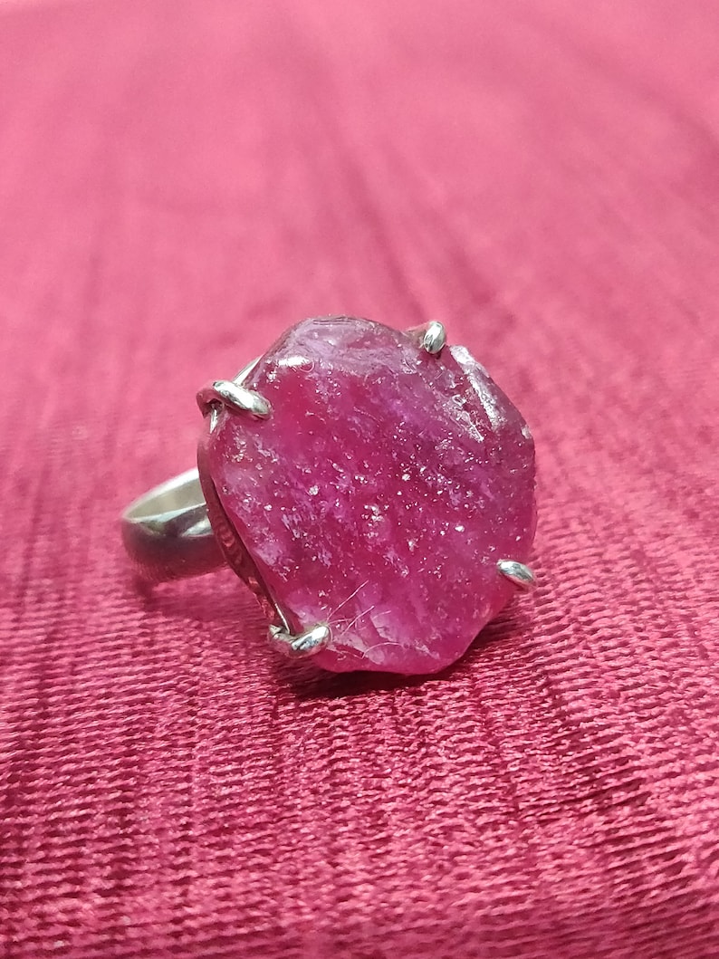 Pode incluir: Um anel de prata com uma grande gema de rubi bruto. O rubi &eacute; de cor rosa intenso e tem uma textura &aacute;spera e natural.