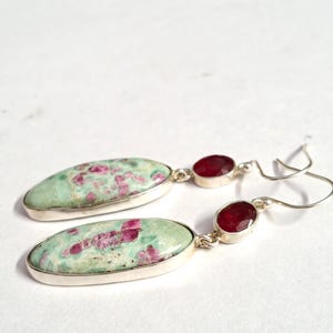 Pu&ograve; includere: Un paio di orecchini in argento. Ogni orecchino presenta una grande pietra ovale verde chiaro con inclusioni rosa, abbinata a una pietra rosso scuro pi&ugrave; piccola, di forma ovale. Gli orecchini sono incastonati in argento.