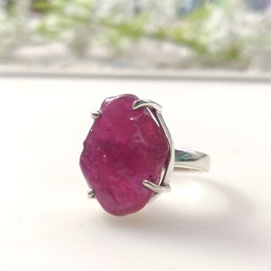 May include: A silver ring featuring a large, raw, pink ruby gemstone. The ruby is set in a simple, prong setting.