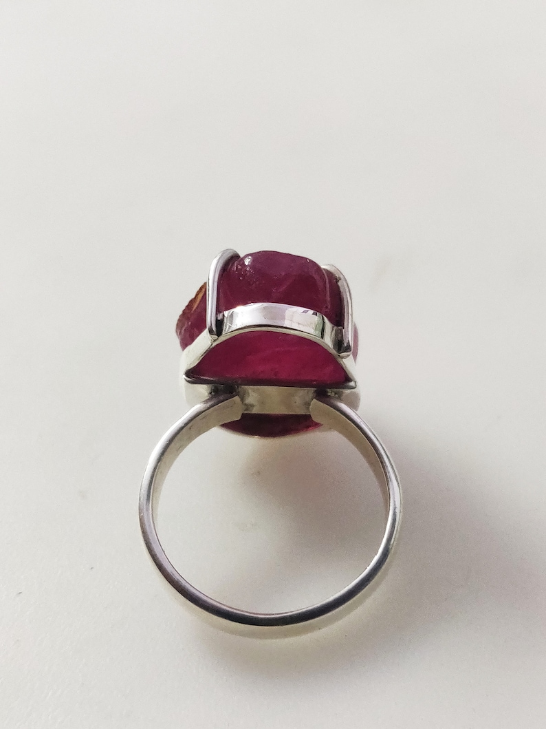 May include: A silver ring featuring a large, faceted, pink gemstone set in a bezel setting.