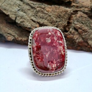Peut inclure: Une bague en argent avec une pierre précieuse rouge et blanche. La pierre précieuse est sertie dans une bélière en argent et a une surface texturée.