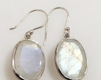 May include: A pair of silver earrings with oval-shaped moonstone gemstones. The stones have a white iridescent sheen.