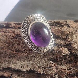 Könnte beinhalten: Ein silberner Ring mit einem verzierten Design, das einen großen, ovalen Amethyst-Edelstein zeigt.