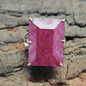 May include: A silver ring with a large, rectangular, deep red gemstone. The gemstone is set in a prong setting.