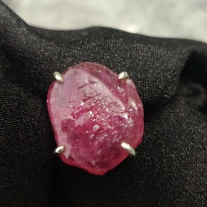 Pode incluir: Uma grande gema de rubi rosa facetada engastada em uma garra de prata.