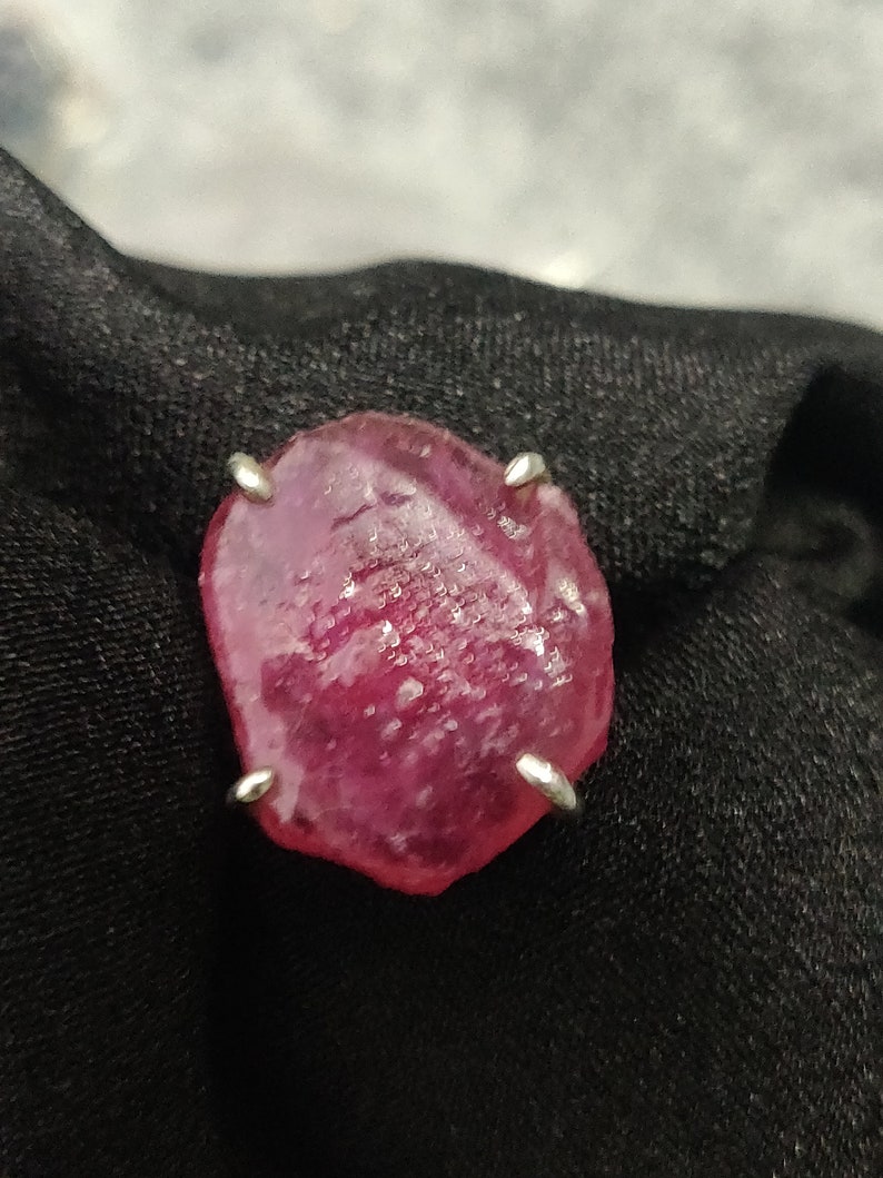 Pode incluir: Uma grande gema de rubi rosa facetada engastada em uma garra de prata.