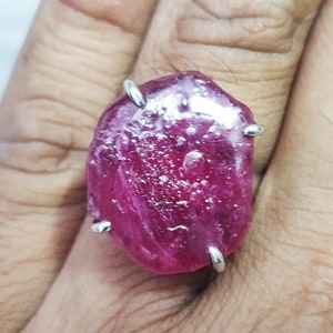 Pode incluir: Um anel com uma grande gema de rubi oval rosa engastada em uma banda de prata. O rubi tem um aspecto &aacute;spero e natural e &eacute; rodeado por quatro garras de prata.
